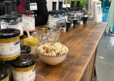 Messe- oder Marktstand mit Produkten der Ostsee-Probiotika GmbH, Stand aus dunklem Holz, darauf Flaschen mit Kräuterbaerry und Gläser mit Kräuterbaerchen Senf sowie schwarze Messbecher aus Metall